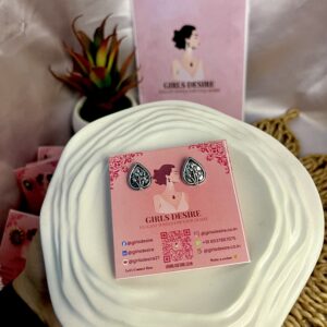 The stud earring shown is a round, oxidized metal piece featuring a dual-tone design. It has a circular shape with a central golden bead or stone, surrounded by intricate patterns and textures.